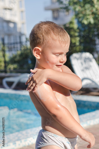 Photo: Little boy applying suntan lotion to his skin Little boy applying suntan lotion to his skin
