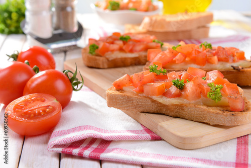 Photo: Delicious bruschetta with tomatoes on cutting board close-up Delicious bruschetta with tomatoes on cutting board close-up