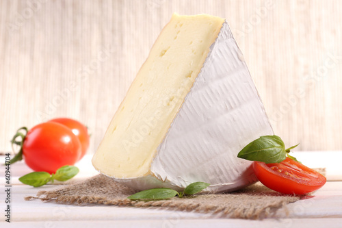 Photo: Tasty Camembert cheese with basil and tomatoes, on wooden table Tasty Camembert cheese with basil and tomatoes, on wooden table