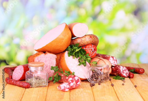Photo: Lot of different sausages on wooden table on natural background Lot of different sausages on wooden table on natural background