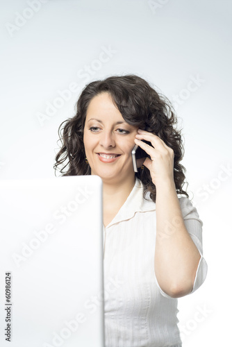 Photo: Young woman in front of laptop talking on the phone Young woman in front of laptop talking on the phone