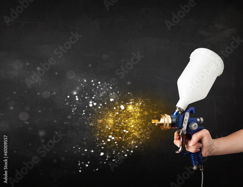 Photo: Worker with airbrush painting with glowing golden paint Worker with airbrush painting with glowing golden paint