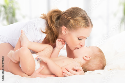 Photo: happy family mother and baby having fun playing, laughing on bed happy family mother and baby having fun playing, laughing on bed