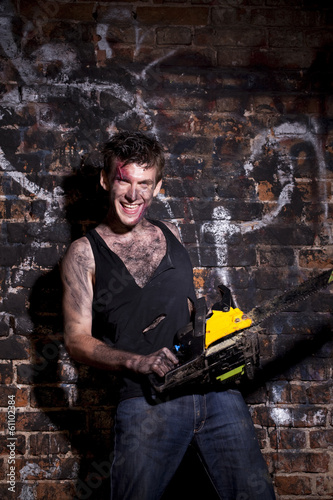 Photo: Horrific madman on a dark background and chainesaw Horrific madman on a dark background and chainesaw