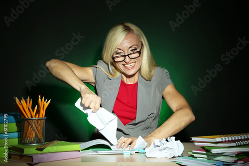 Photo: Wicked teacher sitting at table on dark colorful background Wicked teacher sitting at table on dark colorful background