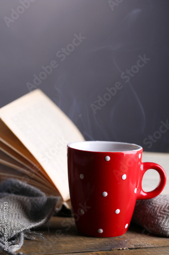 Photo: Cup of hot tea with book and plaid on table on gray background Cup of hot tea with book and plaid on table on gray background