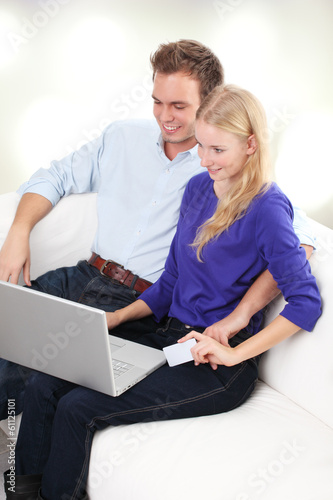 Photo: Happy young couple using laptop in living room Happy young couple using laptop in living room