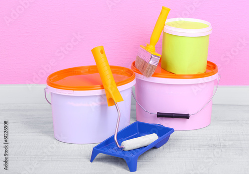 Photo: Paints, roll and paintbrush on floor in room on wall background Paints, roll and paintbrush on floor in room on wall background