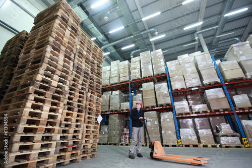 Photo: worker,hand pallet truck, stack of wooden pallets in storehouse worker,hand pallet truck, stack of wooden pallets in storehouse