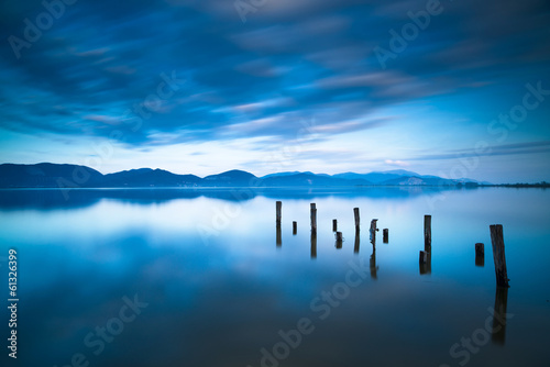 Photo: Wooden pier or jetty remains on a blue lake sunset and sky refle Wooden pier or jetty remains on a blue lake sunset and sky refle