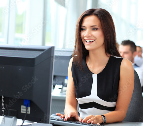 Photo: Casual businesswoman using laptop in office, sitting at desk Casual businesswoman using laptop in office, sitting at desk