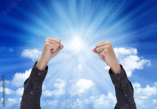 Photo: Man hand with a fist, isolated on blue sky background Man hand with a fist, isolated on blue sky background