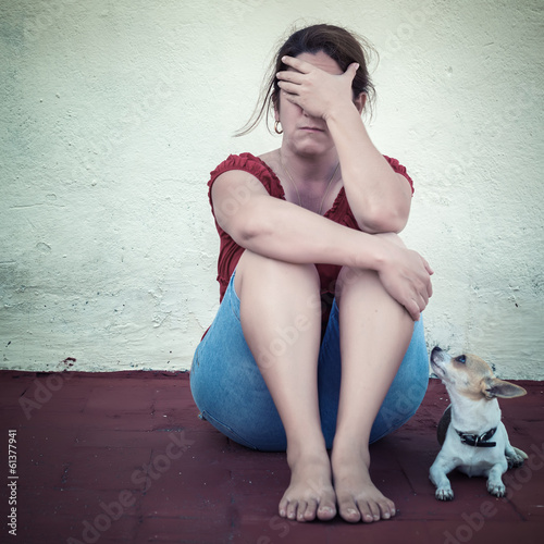 Photo: Sad woman crying with a small dog besides her Sad woman crying with a small dog besides her