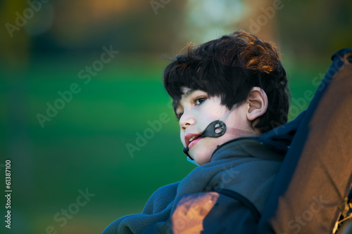 Photo: Handsome disabled boy in wheelchair at park, quiet expression Handsome disabled boy in wheelchair at park, quiet expression