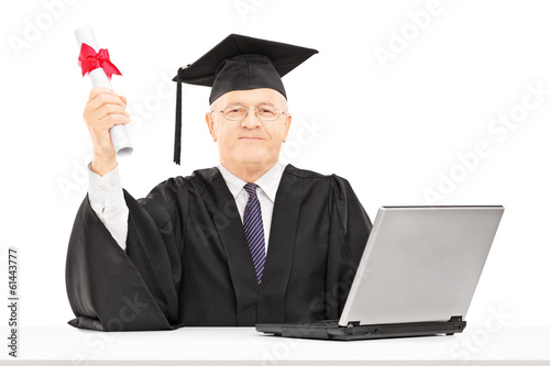 Photo: Mature man in graduation gown posing with diploma and laptop on Mature man in graduation gown posing with diploma and laptop on