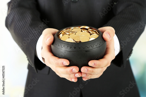 Photo: Ceramic pot with golden coins in male hands, on light Ceramic pot with golden coins in male hands, on light