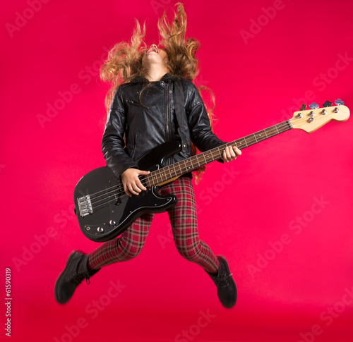 Photo: Blond Rock and roll girl with bass guitar jump on red Blond Rock and roll girl with bass guitar jump on red