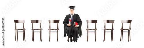 Photo: Excited college student holding diploma, seated on wooden chair Excited college student holding diploma, seated on wooden chair