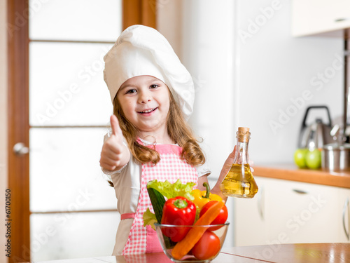 Photo: kid girl weared as cook with vegetables at kitchen kid girl weared as cook with vegetables at kitchen