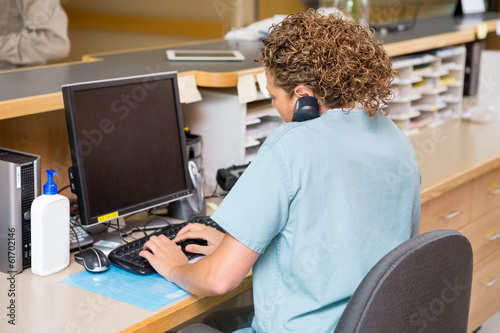 Photo: Nurse Answering Telephone While Working On Computer At Reception Nurse Answering Telephone While Working On Computer At Reception