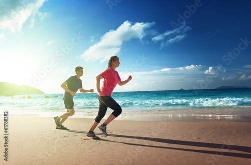 Photo: Man and women running on tropical beach at sunset Man and women running on tropical beach at sunset