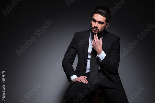 Photo: pensive fashion man sits on stool and looks away pensive fashion man sits on stool and looks away