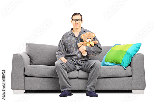 Photo: Young man in pajamas sitting on sofa with teddy bear Young man in pajamas sitting on sofa with teddy bear