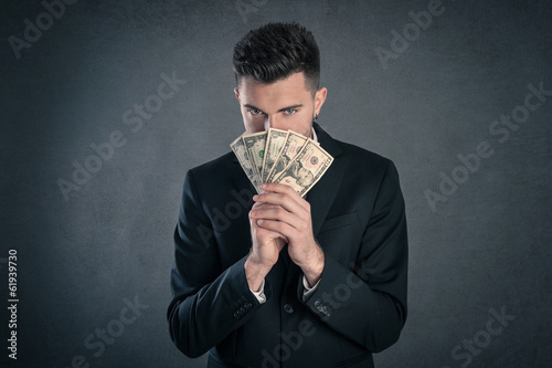 Photo: Man hiding behind dollars banknotes with furtive expression agai Man hiding behind dollars banknotes with furtive expression agai