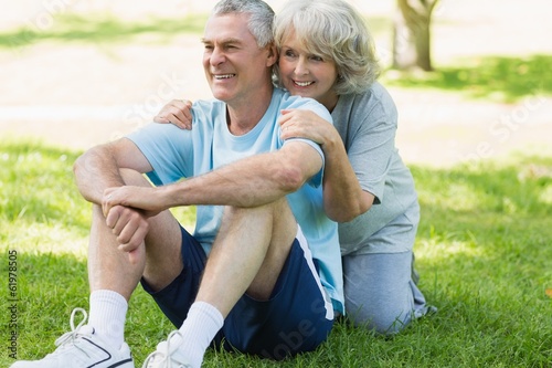 Photo: Smiling mature couple sitting on grass at park Smiling mature couple sitting on grass at park
