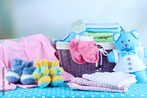 Photo: Pile of baby clothes in basket, on table on color background Pile of baby clothes in basket, on table on color background