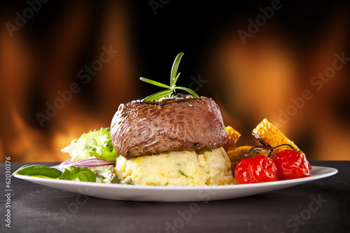 Photo: Fresh beef steak on black stone and fire Fresh beef steak on black stone and fire