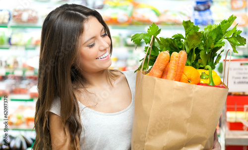Photo: Young woman holding a shopping bag full of vegetables Young woman holding a shopping bag full of vegetables