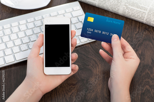 Photo: female hands holding phone and credit card over the table in off female hands holding phone and credit card over the table in off