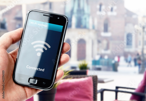 Photo: Hand holding smartphone with wi-fi connection in cafe Hand holding smartphone with wi-fi connection in cafe