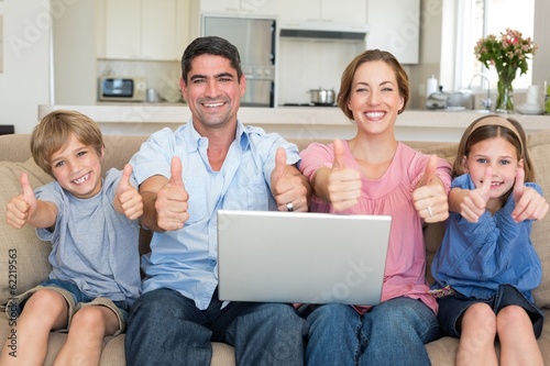 Photo: Family with laptop gesturing thumbs up on sofa Family with laptop gesturing thumbs up on sofa