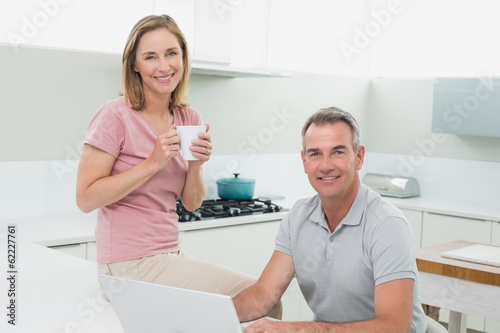 Photo: Portrait of a happy couple using laptop in kitchen Portrait of a happy couple using laptop in kitchen