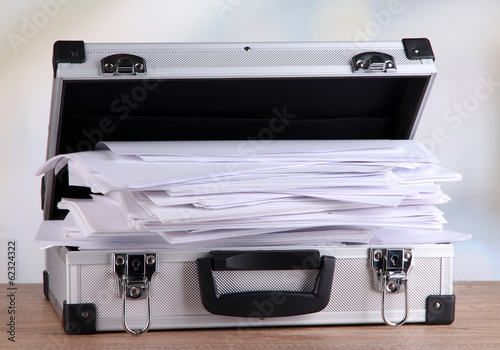 Photo: Briefcase full of papers, on wooden table, on light background Briefcase full of papers, on wooden table, on light background