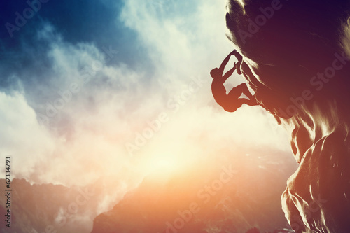 Fototapeta A silhouette of man climbing on rock, mountain at sunset.