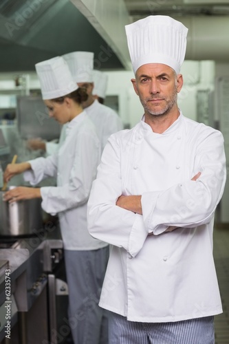 Photo: Serious chef looking at camera with team working behind Serious chef looking at camera with team working behind