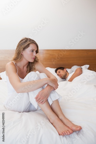 Photo: Sad woman with man sleeping in background Sad woman with man sleeping in background
