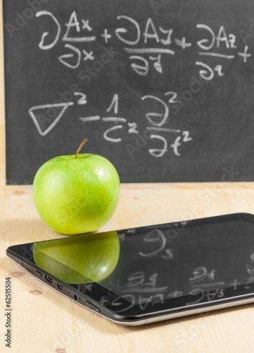 Photo: tablet pc and green apple in front of blackboard on wood table tablet pc and green apple in front of blackboard on wood table