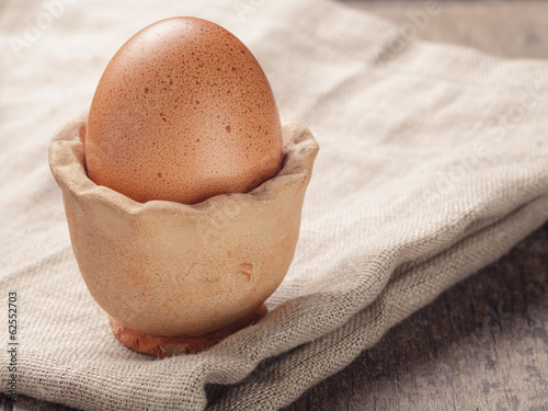 Photo: brown egg in handmade holder on rustic table brown egg in handmade holder on rustic table