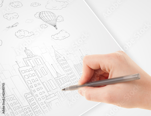 Photo: A person drawing sketch of a city with balloons and clouds on a A person drawing sketch of a city with balloons and clouds on a