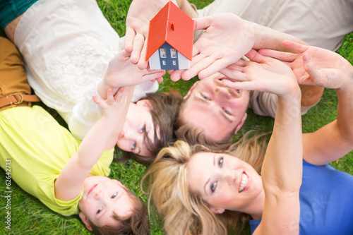 Photo: Familie liegt auf der wiese mit haus in der hand Familie liegt auf der wiese mit haus in der hand