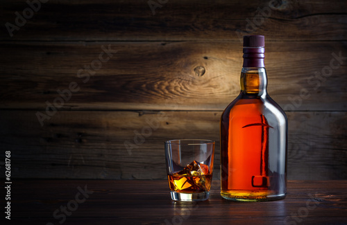 Fototapeta bottle and glass of whiskey with ice on a wooden background
