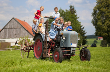 Photo: Deutschland, Bayern, Frau mit einer Gruppe von Kindern auf alten Traktor sitzt vor Bauernhaus Deutschland, Bayern, Frau mit einer Gruppe von Kindern auf alten Traktor sitzt vor Bauernhaus