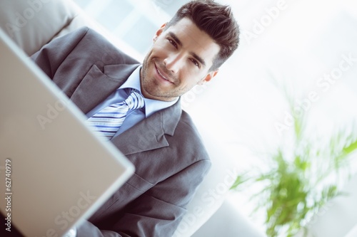 Photo: Handsome businessman sitting on couch using his laptop Handsome businessman sitting on couch using his laptop