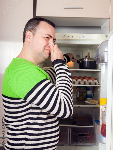 Photo: Guy looking for something in pan near fridge Guy looking for something in pan near fridge