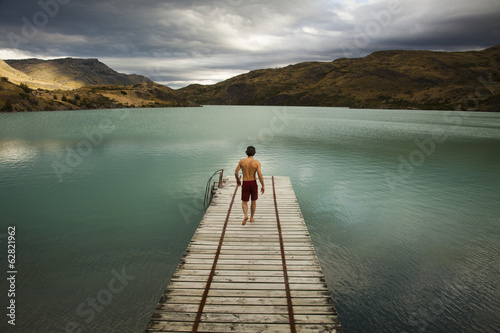 Photo: A young man walking down a wooden pier, towards calm lake surrounded by mountains in Torres del Paine National Park, Chile. A young man walking down a wooden pier, towards calm lake surrounded by mountains in Torres del Paine National Park, Chile.
