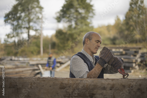 Foto: Two men working in a reclaimed timber yard. One using a tool to remove metals from a reclaimed piece of timber. Two men working in a reclaimed timber yard. One using a tool to remove metals from a reclaimed piece of timber.